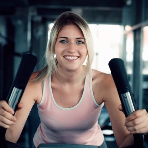 Indoor cycling jako przygotowanie do sezonu rowerowego Uśmiechnięta kobieta na rowerze stacjonarnym