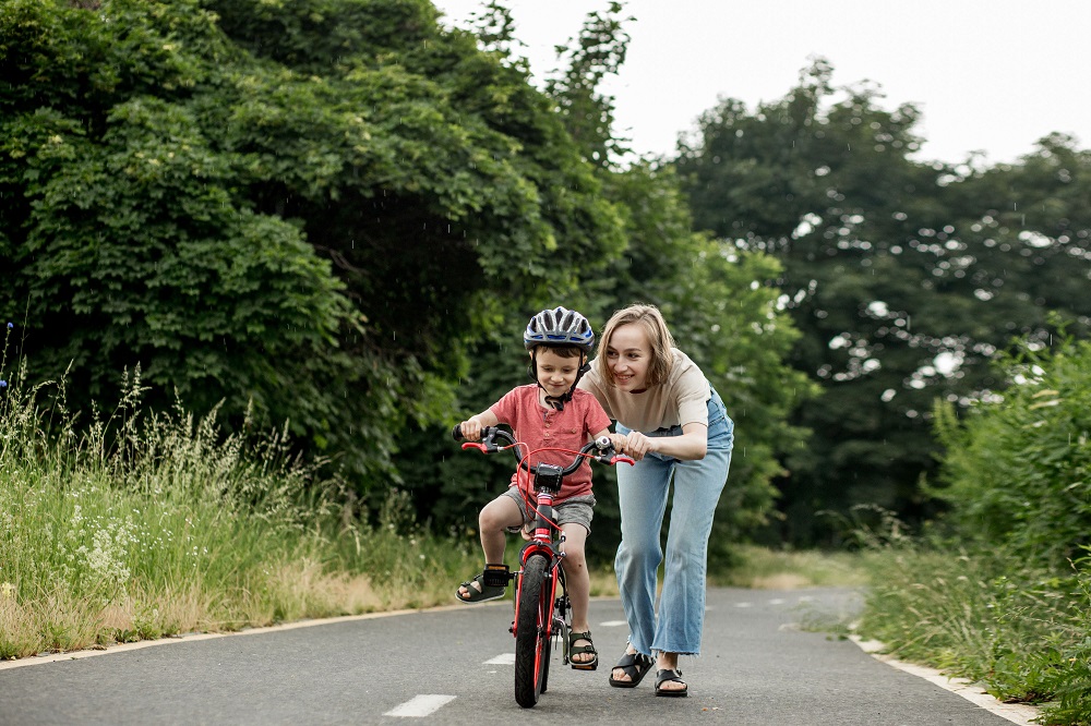Kobieta przytrzymuje dziecko uczące się jazdy na rowerze